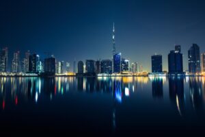 Dubai skyline at night with illuminated skyscrapers and reflections on the water.